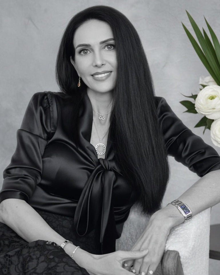 Woman in a black dress sitting with a vase of white flowers in the background